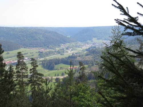 Malerische Aussicht über ein grünes Tal mit Dorf und umgebenden Wäldern.