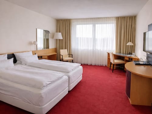 Elegantes Hotelzimmer mit zwei Einzelbetten, rotem Teppich und modernen Holzmöbeln.