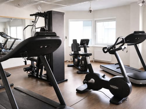 Innenansicht eines modernen Fitnessstudios mit Laufband, Hometrainer und Kraftgerät.