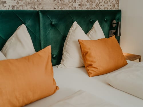 Elegantes Bett mit grüner Polsterung und orangefarbenen Kissen
