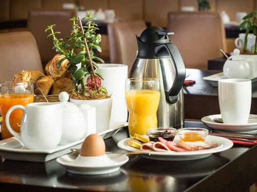 Reichhaltiges Frühstück mit Brötchen, Orangensaft, Teekanne und Ei.