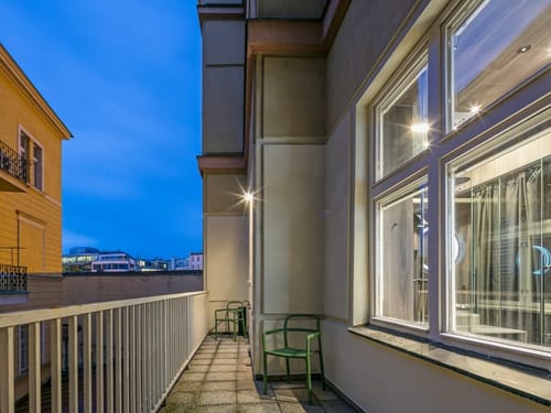 Gemütlicher Hotelbalkon in der Abenddämmerung mit grünen Stühlen, weißem Geländer und beleuchtetem Stadtblick