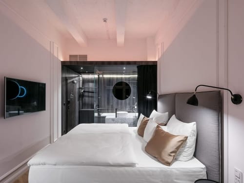 Hotelzimmer mit offenem Badezimmer, Glasdusche und elegantem Doppelbett in modernem Boutique-Design