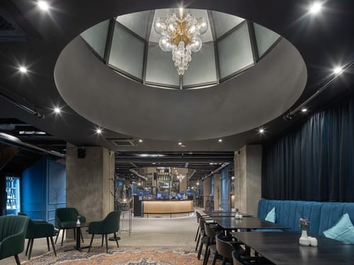Großzügiger Lobby mit einem markanten runden Deckenoberlicht, an dem ein kunstvoller Glaskronleuchter hängt.