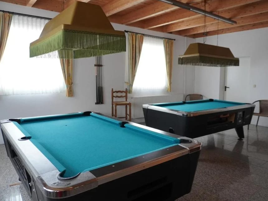 Zwei Billardtische in einem hellen Raum mit modernen Leuchten und Holzbalkendecke.