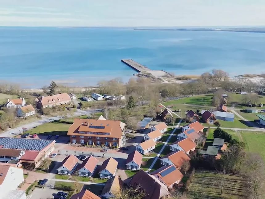 Luftaufnahme eines Dorfes an der Küste mit roten Dächern und blauem Meer im Hintergrund.