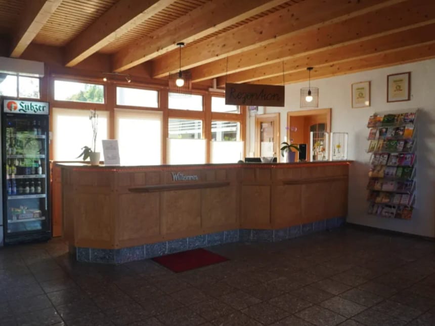 Empfangsbereich eines Hotels mit hölzernem Tresen, Getränkekühlschrank und Prospekthalter