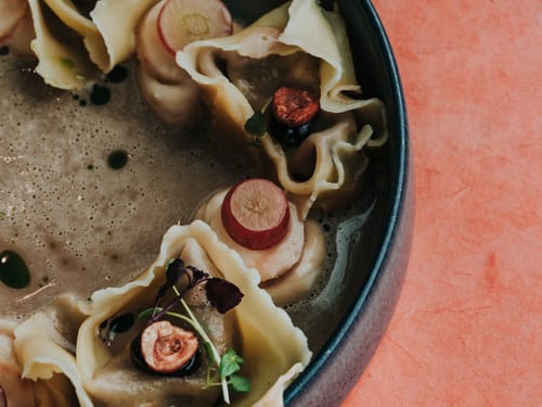 Nahaufnahme von gefüllten Pasta-Taschen in Brühe mit Kräutergarnitur und Radieschenscheiben