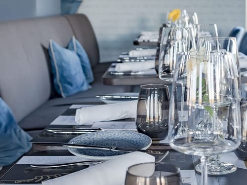 Elegante Tischdekoration in einem gehobenen Restaurant mit Kristallgläsern und blauen Kissen.