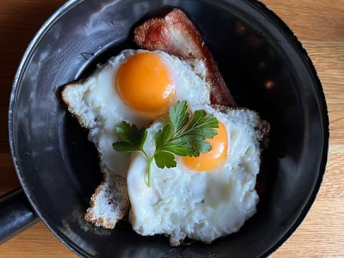 Gebratene Eier mit Speck in einer schwarzen Pfanne