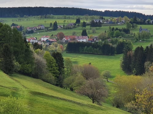 Malerische Landschaft in Deutschland mit Hügeln, Wäldern und einem Dorf im Hintergrund.