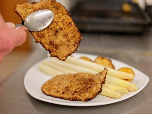 Ein Teller mit paniertem Schnitzel, weißen Spargelstangen und Kartoffeln.