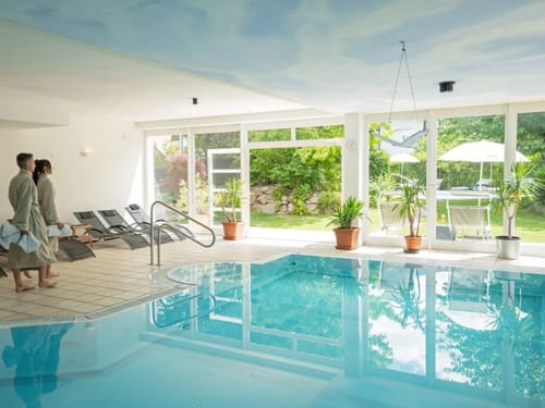 Innenansicht eines Wellnessbereichs mit Pool und Blick auf den Garten.