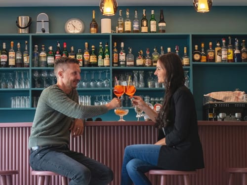 Zwei Personen stoßen mit Cocktails in einer stilvollen Bar an.