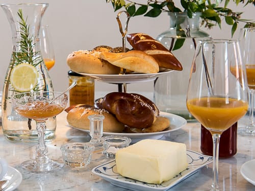 Elegantes Frühstücksarrangement mit Gebäck, Butter und frischem Orangensaft auf Mamortisch.