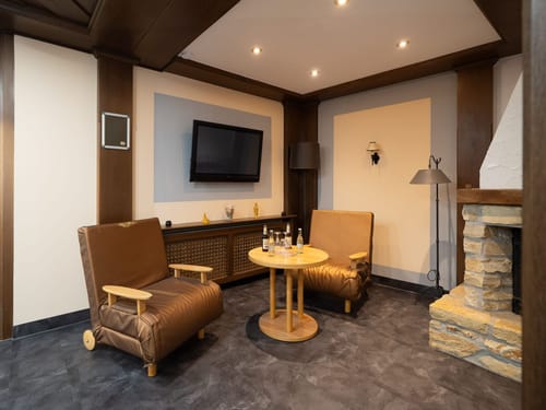 Gemütliche Sitzecke mit Sesseln, einem Tisch, Wandfernseher und Kamin in modernem Raumdesign.