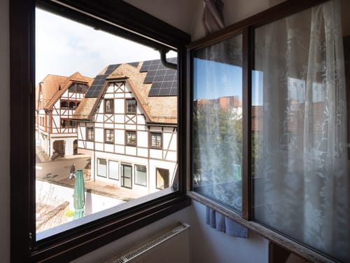 Blick aus einem Fenster auf ein traditionelles Fachwerkhaus mit Solarpanels.