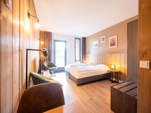 Gemütliches Hotelzimmer mit Holzelementen, Doppelbett und moderner Beleuchtung.