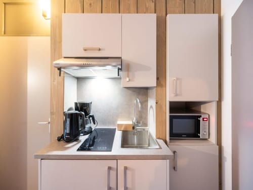 Moderne kleine Küche mit Kochfeld, Spüle, Mikrowelle, Wasserkocher und Kaffeemaschine.