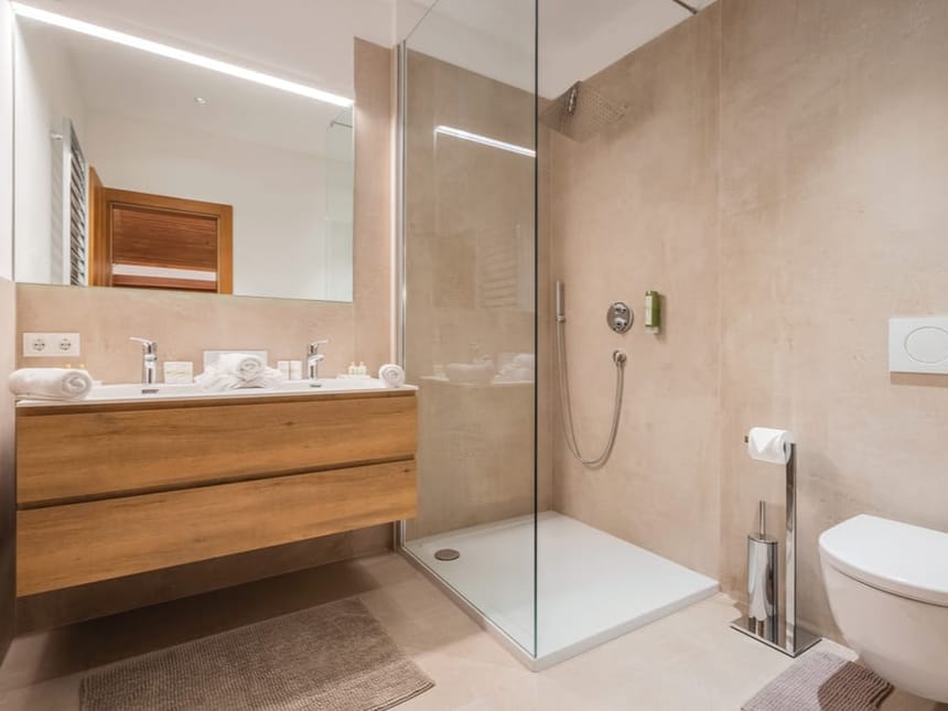 Hochwertiges Badezimmer mit ebenerdiger Glasdusche, schwebendem Holzunterschrank und stilvoller Beleuchtung in modernem Beige-Design