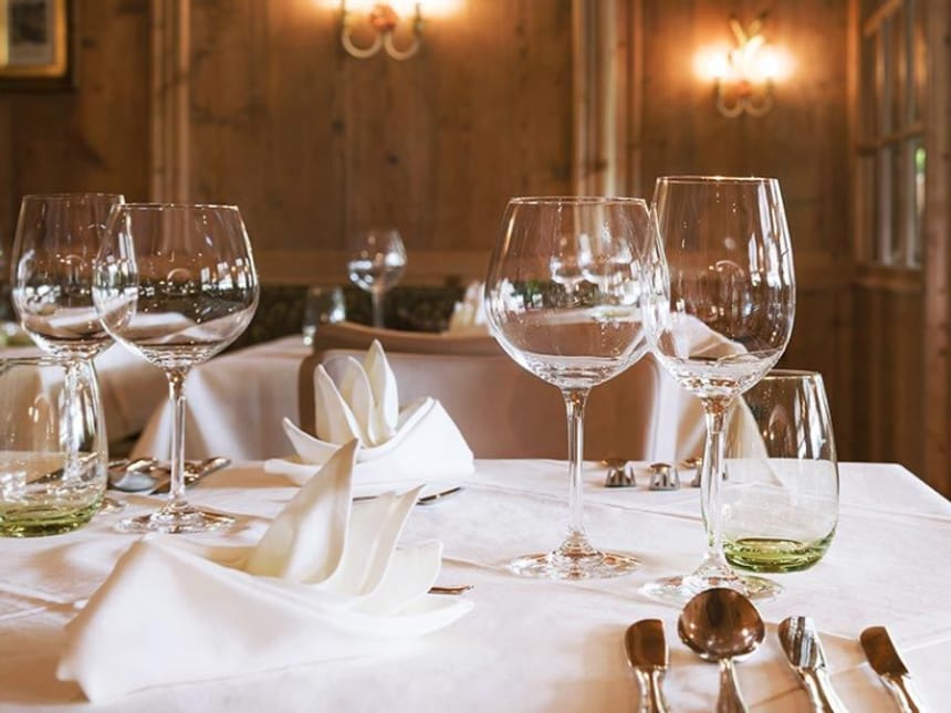 Festlich gedeckter Tisch mit Weingläsern und Stoffservietten in einem rustikalen Restaurant mit Holzvertäfelung