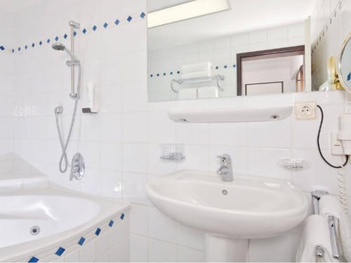 Gepflegtes Hotelbadezimmer mit Badewanne, Dusche, Waschbecken und Spiegel in klassisch-weißem Design mit blauen Akzenten