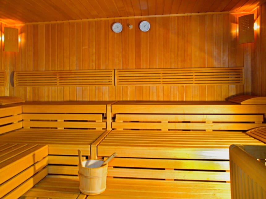 Einladender Innenraum einer finnischen Sauna mit Holzbänken auf mehreren Ebenen, Saunakübel und Messinstrumenten für Temperatur und Luftfeuchtigkeit