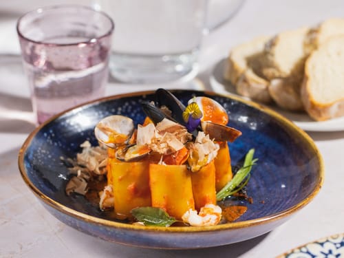 Saftige Röhrennudeln mit Meeresfrüchten, verfeinert mit Meeresfrüchten und dekorativer Blüte, serviert in einem stilvollen Restaurant