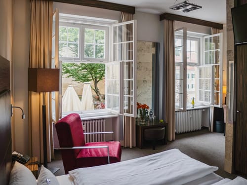 Modernes Hotelzimmer mit offenem Fenster, Sessel und Gartenblick