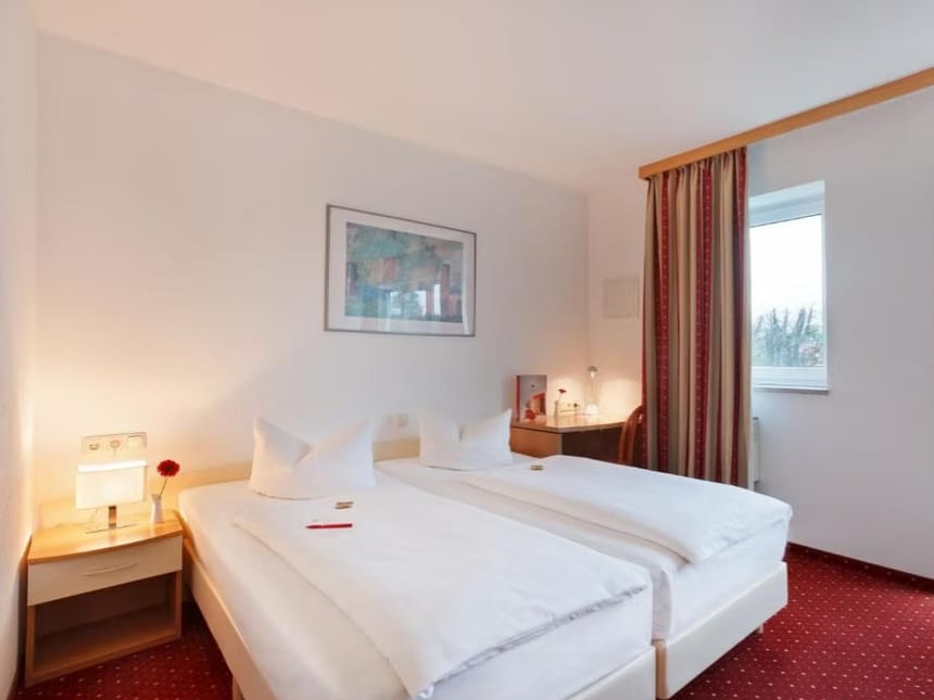 Modernes Hotelzimmer mit zwei Einzelbetten, Schreibtisch und Fenster.
