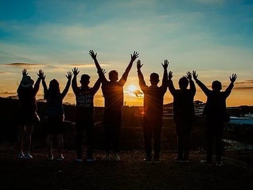 Gruppe hebt Hände beim Sonnenuntergang – Gemeinschaft und Freiheit