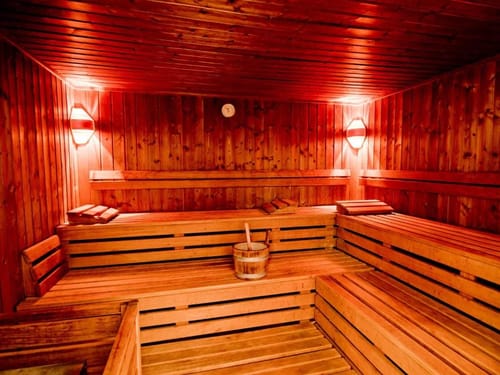 Holzsauna mit warmem Rotlicht, Mehrstufen-Sitzbänken und einem traditionellen Aufgusseimer
