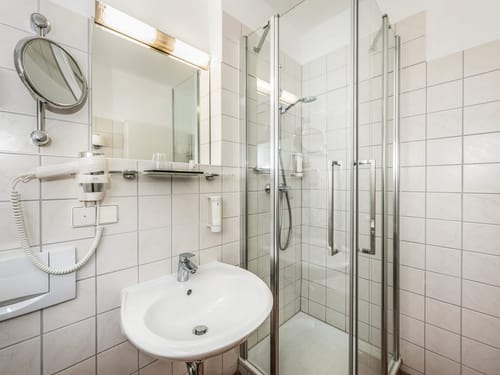 Helles Badezimmer im Hotelzimmer mit Glasdusche, Waschbecken und modernem Zubehör