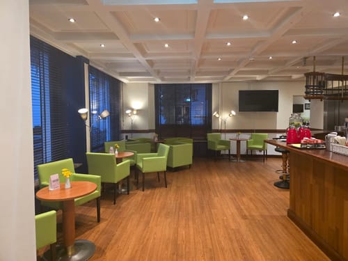 Gemütliche Lounge eines Hotels mit grünen Sesseln, Holztheke und stilvoller Kassettendecke