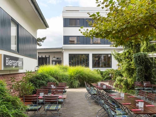 Der Biergarten des Hotels lädt mit schattenspendenden Bäumen, gepflegten Holzmöbeln und grüner Umgebung zum entspannten Verweilen im Freien ein