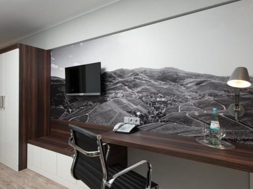Hotelzimmer mit modernem Arbeitsbereich und dekorativer Schwarz-Weiß-Fototapete einer Weinberglandschaft