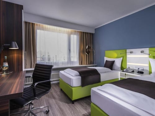 Komfortables Zweibettzimmer mit modernem Design, grünen Bettrahmen, blauer Wandgestaltung und vollständig ausgestattetem Arbeitsbereich