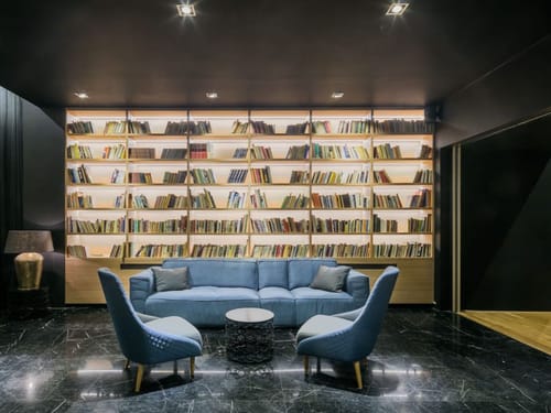Bibliothekslounge mit beleuchtetem Raumteiler-Bücherregal und blauer Polstergarnitur – modernes Interior-Design auf höchstem Niveau