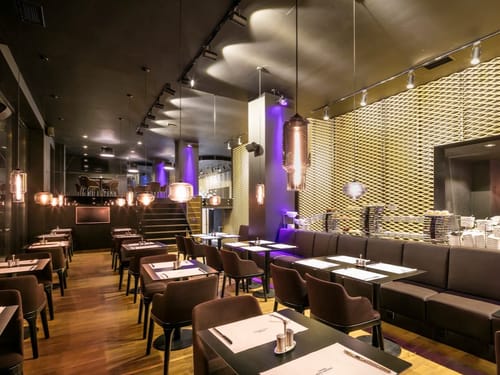 Exklusives Restaurant-Ambiente mit Kupfer-Pendelleuchten, violettem Lichtakzent und goldener Wandverkleidung