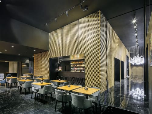 Modernes Luxusrestaurant mit auffälliger goldener Gitterfassade, edlem Bartresen und stilvoll eingedeckten Tischen in dunklem Ambiente.