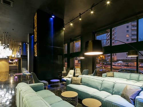 Hotellobby mit mintgrünen Sofas, schwarzem Interieur und abendlicher Stadtansicht durch Panoramafenster