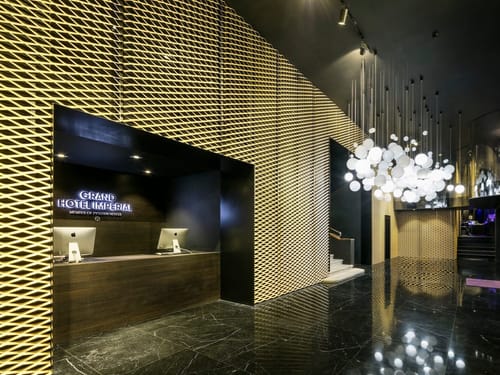Rezeption des Grand Hotel Imperial mit goldener Gitterfassade, hölzernem Tresen und dekorativem Kugelleuchter in der Lobby