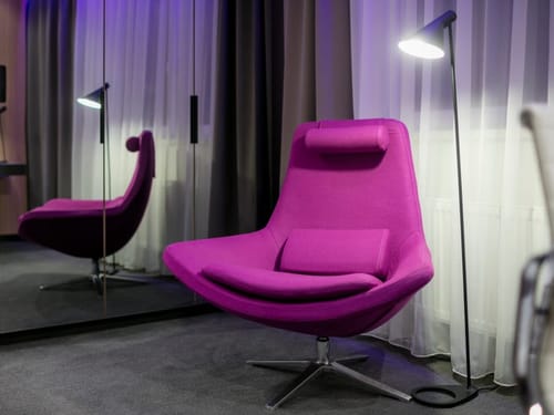Magenta-Loungesessel mit Stehlampe in einem modernen Hotelzimmer mit stimmungsvoller Beleuchtung und Spiegelfron