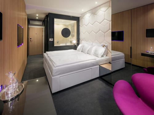 Hotelzimmer mit weißem Boxspringbett, Wabenstruktur-Kopfteil und auffälligem pinken Sessel