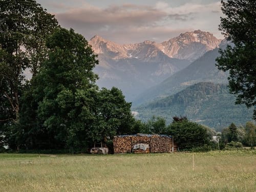 Idyllische Alpenlandschaft mit Holzstapel und Bergpanorama im Sonnenuntergang