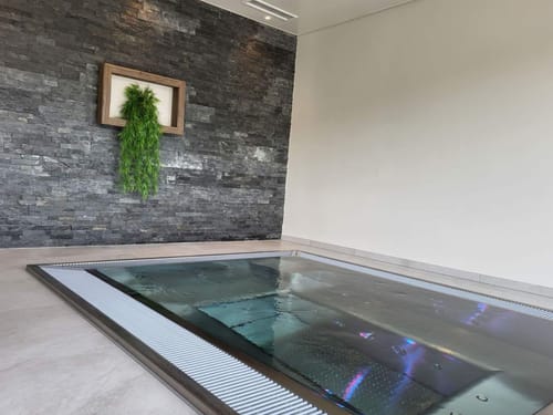 Hallenbad mit versenktem Glaspool und Natursteinoptik