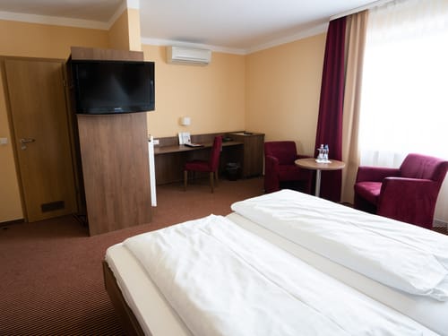 Komfortables Hotelzimmer mit modernem Design, ausgestattet mit einem Doppelbett, einem Schreibtisch, einem Flachbildfernseher und einer gemütlichen Sitzgelegenheit.