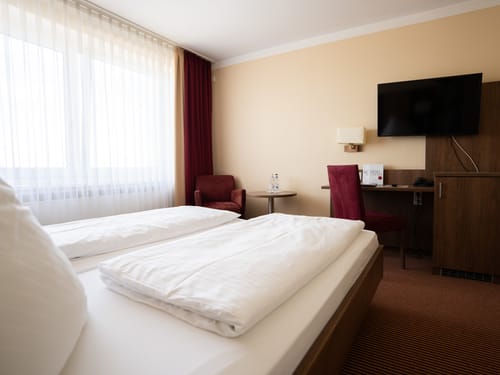 Hotelzimmer mit Doppelbett, Flachbildfernseher, Schreibtisch und gemütlicher Sitzecke.