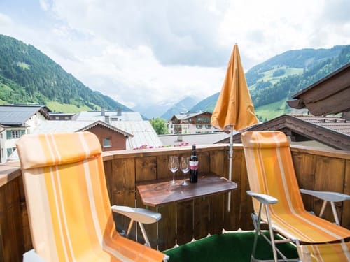 zwei Liegestühle, Sonnenschirm und eine Flasche Rotwein mit zwei Gläsern auf der Terrasse